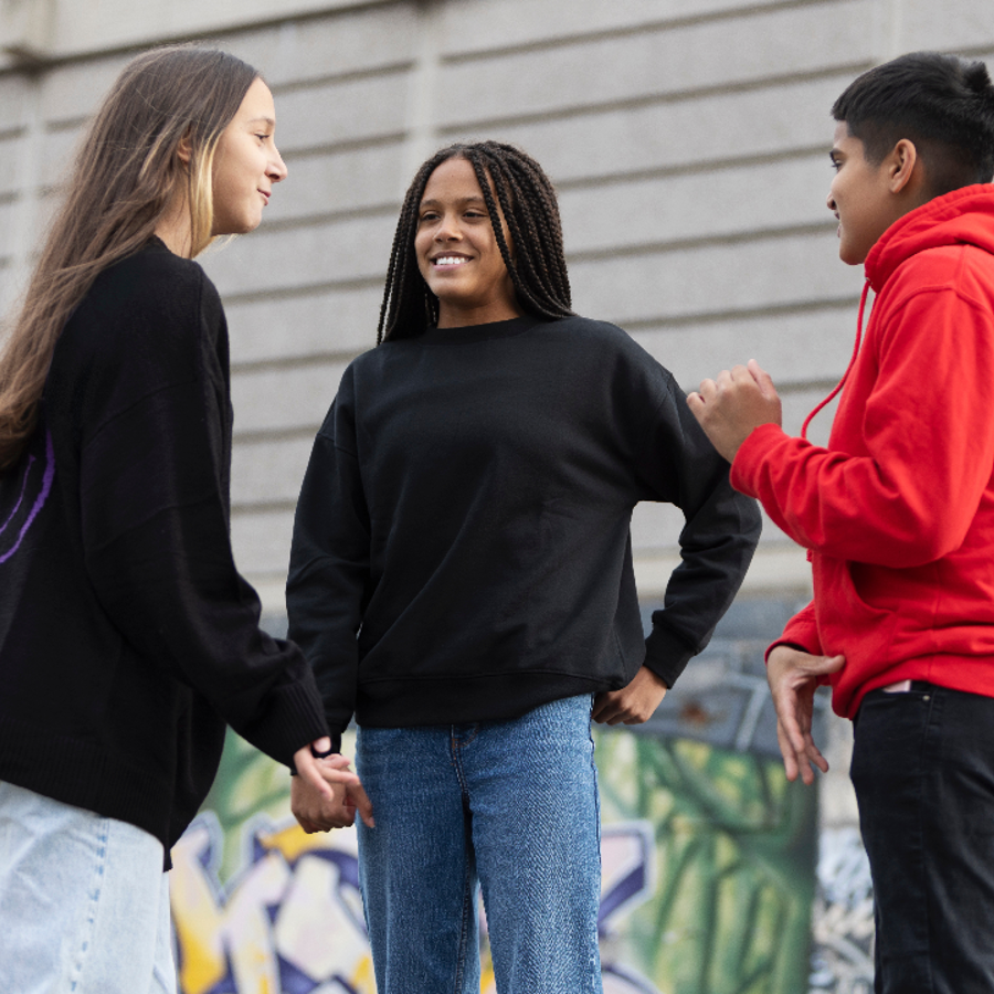 Three young people smiling and chatting together in front of a colourful graffiti wall